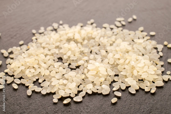 Fototapeta Round grain uncooked rice on slate stone, macro.