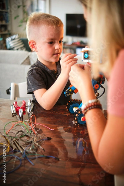 Obraz A beautiful moment shared by a mother and son as they work together with various tools to assemble a robot, painting a picture of love and collaboration on an autumn day.