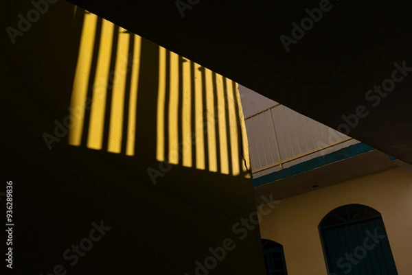 Fototapeta Sunlight casts dramatic shadows on a yellow wall, creating a striking geometric pattern