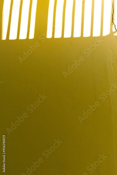 Fototapeta Soft sunlight creates gentle shadows on a yellow wall, forming a minimalist pattern