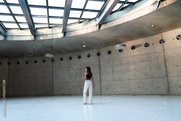 Fototapeta Woman walking in a large museum area with empty walls. Young woman walking in the empty gallery