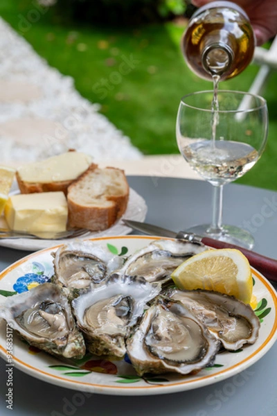 Fototapeta Plate with fresh live oysters with citron, bread, butter and white wine served at restaurant in oyster-farming village, Arcachon bay, Gujan-Mestras port, France