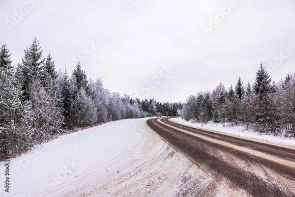 Fototapeta Beautiful view of winding road through snowy forest with frost-covered trees under overcast sky. Sweden.