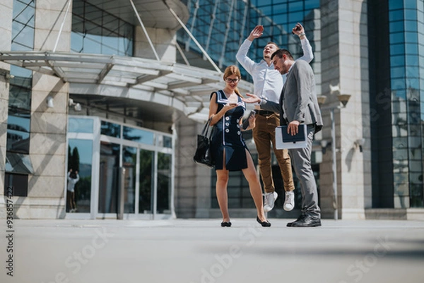 Fototapeta A joyful business team celebrating success outside a modern office building, representing teamwork, achievement, and professional excitement on a sunny day in the city.