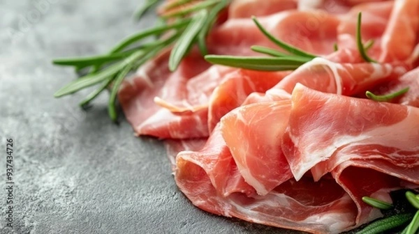 Fototapeta Thinly sliced prosciutto with rosemary sprigs on a black slate background.