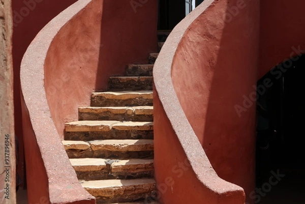 Obraz Vue d'un détail de l'escalier de couleur orangée de la maison des esclaves de l'île de Gorée au Sénégal. Rampe de forme incurvée. Architecture coloniale. Bâtiment rénové et coloré. Avril 2024.