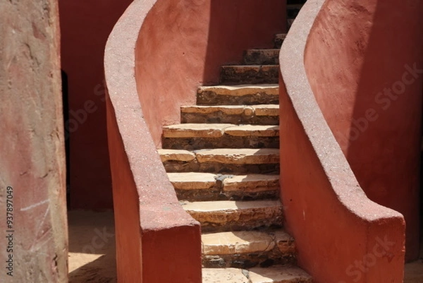 Obraz Vue d'un détail de l'escalier de couleur orangée de la maison des esclaves de l'île de Gorée au Sénégal. Rampe de forme incurvée. Architecture coloniale. Bâtiment rénové et coloré. Avril 2024.