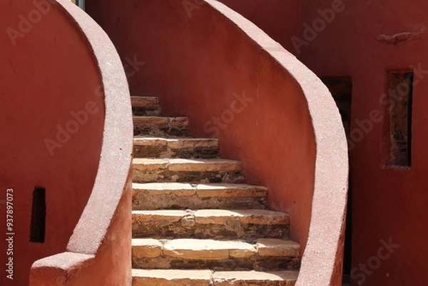 Obraz Vue d'un détail de l'escalier de couleur orangée de la maison des esclaves de l'île de Gorée au Sénégal. Rampe de forme incurvée. Architecture coloniale. Bâtiment rénové et coloré. Avril 2024.