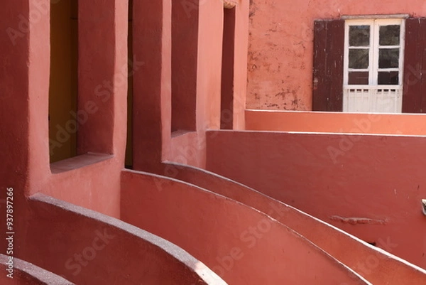 Obraz Vue d'un détail de l'escalier de couleur orangée de la maison des esclaves de l'île de Gorée au Sénégal. Rampe de forme incurvée. Architecture coloniale. Bâtiment rénové et coloré. Avril 2024.