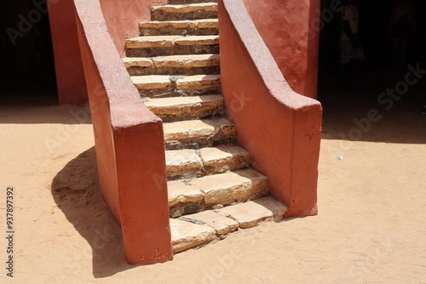Obraz Vue d'un détail de l'escalier de couleur orangée de la maison des esclaves de l'île de Gorée au Sénégal. Rampe de forme incurvée. Architecture coloniale. Bâtiment rénové et coloré. Avril 2024.