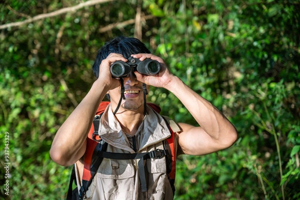 Fototapeta Young Asian man using binoculars exploring forest and enjoying wildlife observation during hiking adventure