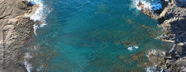 Fototapeta Atlantic ocean with waves and black basalt sand and rocks, view from above from a drone.