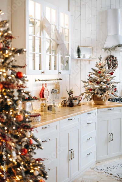 Obraz White kitchen with wooden countertops decorated for Christmas. A small Christmas tree with ornaments, a star on the cabinet, and festive accessories create a cozy holiday atmosphere
