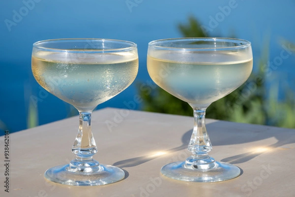 Fototapeta Cold sparkling wine, cava or champagne in two coupe glasses on table with blue sea water view