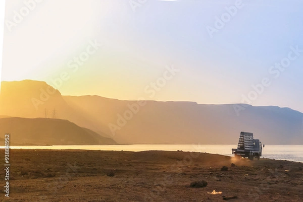 Fototapeta Sunset at Al Ain Al Sokhna, Suez, Egypt, with a truck driving along the beach. Mountains and soft sunlight create a tranquil backdrop