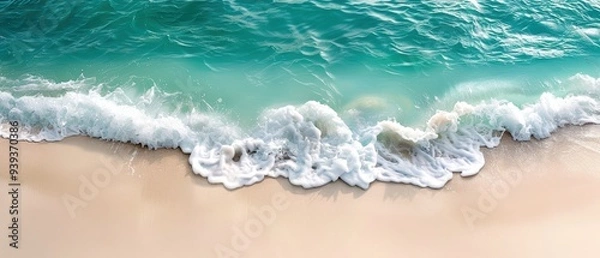 Fototapeta Aerial view of a turquoise ocean wave gently crashing onto a sandy beach, creating a serene and tranquil seaside landscape.