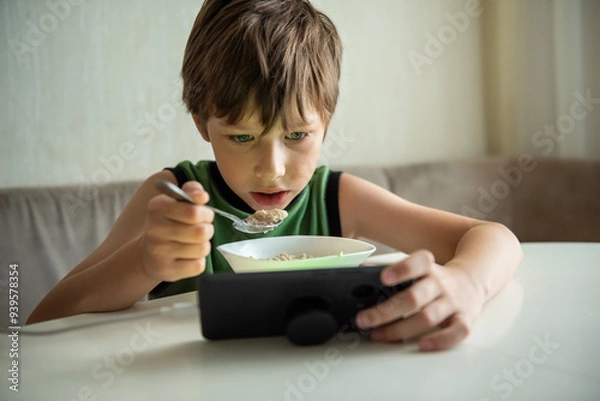 Fototapeta Child boy eats by game. Kid eating and surfing on internet or playing video games on console. Gadget addiction, habit