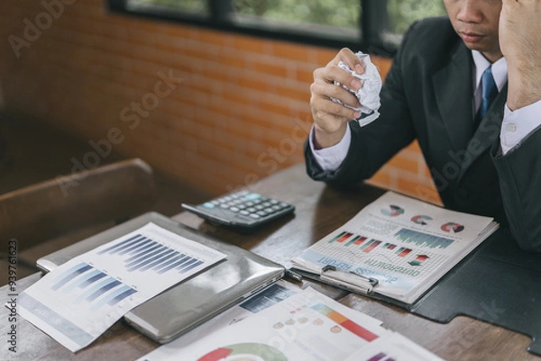 Fototapeta Asian Businessman being depressed by working on the laptop computer in office.Strain,Young business man to think and not Work with stress Pretending to put his hand to the head