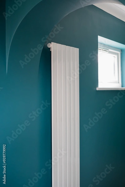 Fototapeta Slim vertical white central heating radiator on a green wall by an arch way and a window in a newly decorated room