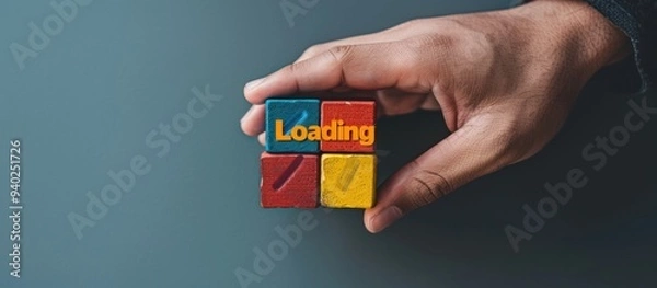 Fototapeta Hand holding colorful block with text "Loading" on grey background. Loading screen concept for web design and mobile app development.