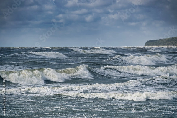 Fototapeta Dramatic ocean waves crashing against the shore under a cloudy sky