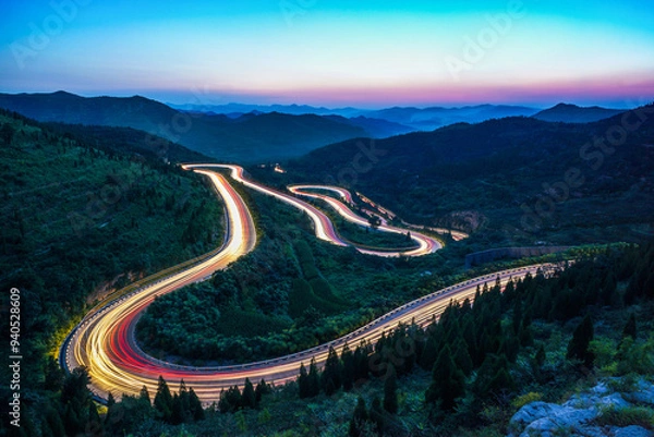 Obraz At night, on the winding mountain road, the car lights form a long stream of light