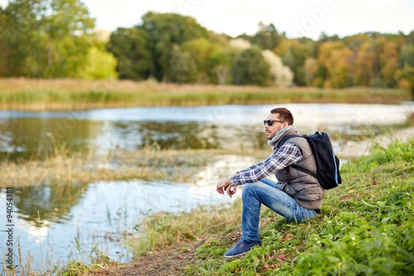 Obraz man with backpack resting on river bank