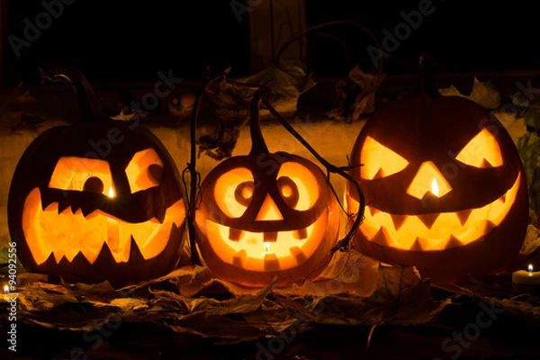 Fototapeta Photo of three pumpkins for Halloween. Embittered, cheerful with a smile and evil pumpkin against autumn leaves and candles