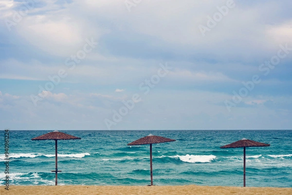 Obraz Еmpty beach with sand, see, sky and three strawy umbrellas in decreasing height, suitable for chart graphically reflecting a decreasing or increasing trend