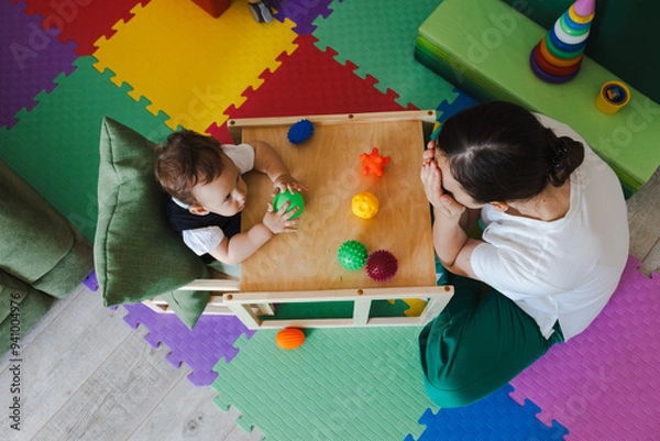 Fototapeta Concentrated boy during SIT classes with educational psychologist holding colored ball for development of sensory sensitivities, top view. Sensory integration therapy