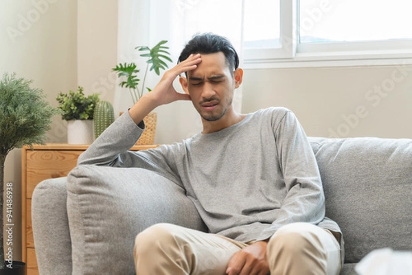 Fototapeta Guy have headache and dizzy sitting on sofa at home