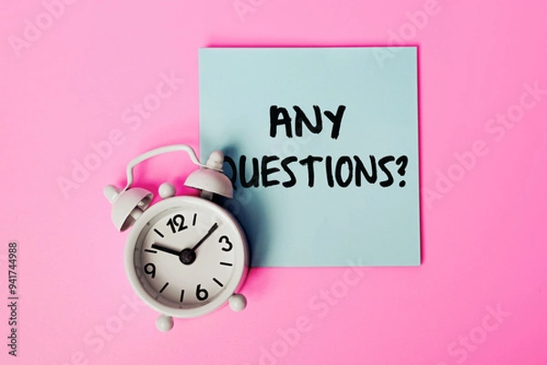 Fototapeta Sticky Note with 'Any Questions?' Written on It, Concept for Q&A Sessions, Inquiries, Customer Support, or Classroom Discussions. White alarm clock and Blue Note on a Pink Background