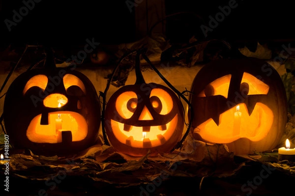 Fototapeta Photo composition from three pumpkins on Halloween. Crying, mad and afraid of some pumpkin against an old window, leaves and candles.