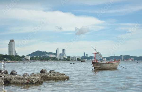 Fototapeta Sunset time at harbor. Beautiful sunset at tropical sea with small fishing boat isolated with cityscape view. Wooden boat with sunrise beach horizon background.