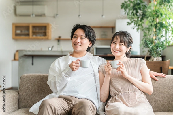 Fototapeta 家のリビング・ソファでくつろぐ仲良しの若い日本人夫婦
