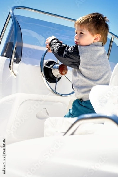 Fototapeta Little child sailor steering a sailboat as captain