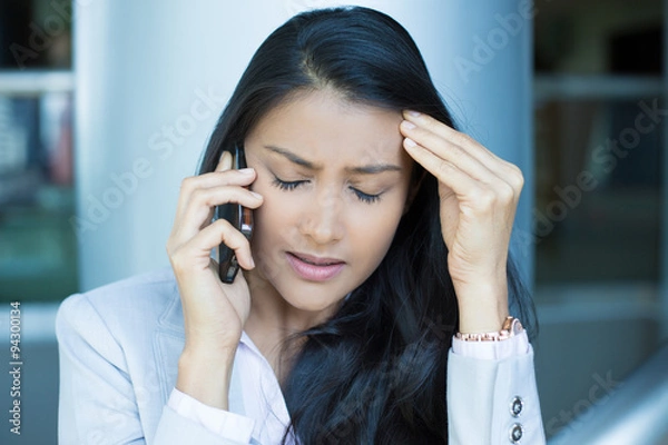 Obraz Closeup portrait, sad, depressed, unhappy worried young woman talking on phone, isolated indoors office background. Negative human emotions, facial expressions, feelings, reaction. Bad news.