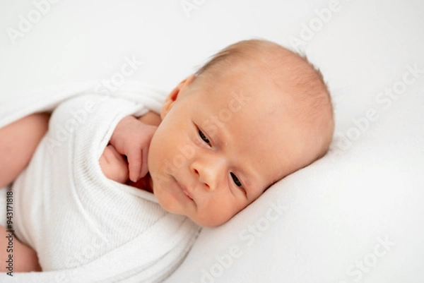 Fototapeta a newborn baby is lying in a diaper on a bed on a white isolated background, a place for text, a small baby boy is sleeping sweetly, a close-up portrait