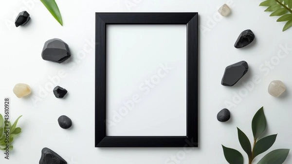 Fototapeta A blank black frame surrounded by various stones and greenery on a light background in a natural setting.
