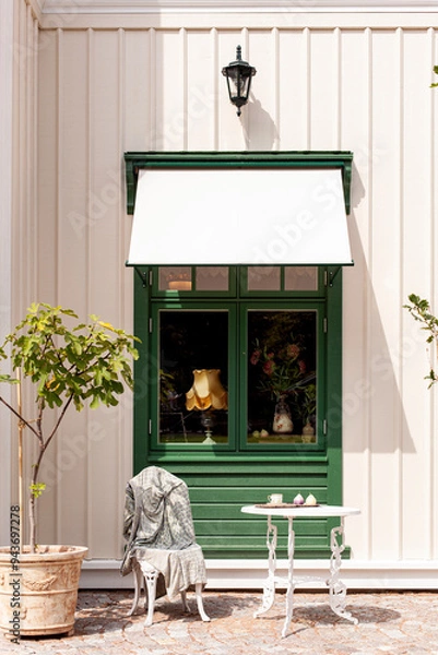 Fototapeta Gemütliche Sitzgruppe vor grünem Fenster. Kleines Kaffee mit Sitzgruppe vor Fenster.
Cozy seating area in front of a green window. Small café with seating area in front of window.
