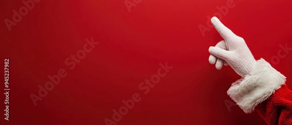 Fototapeta Santa Claus, pointing with the index finger against a solid red background. The hand is positioned at the right edge of the frame, a minimalist composition with a strong Christmas theme. Generative AI