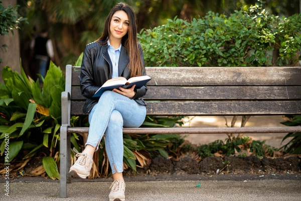 Fototapeta Young woman using a digital tablet sitting on a bench in a park