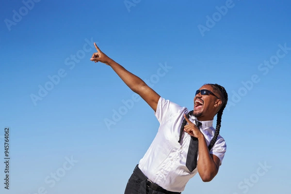 Fototapeta A man in a white shirt and black tie is singing and pointing to the sky