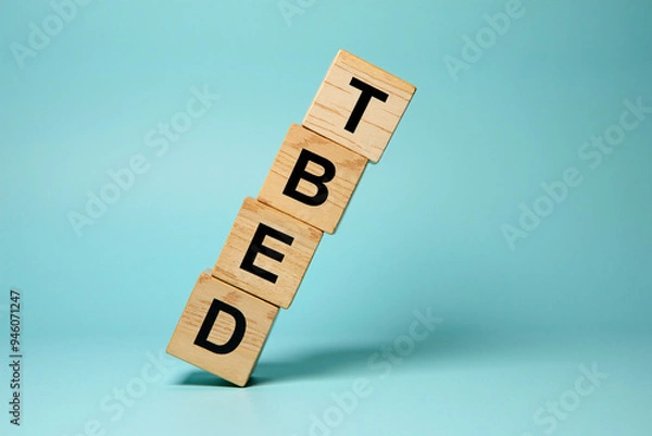 Fototapeta Wooden alphabet blocks piled up to form the word DEBT, leaning, about to fall. Concept on unsustainable debt, collapse of financial system, economy due to high borrowings, unpaid mounting loans.