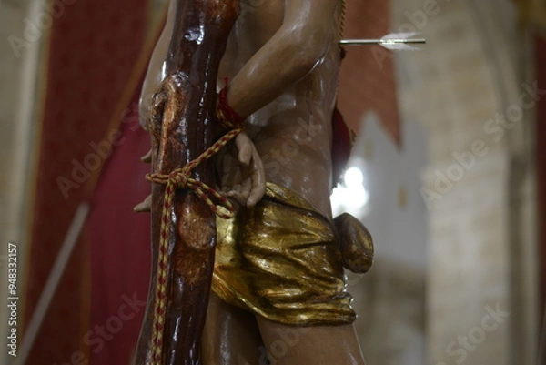 Fototapeta Detail of the Statue of Saint Sebastian of Ferla: Martyrdom, Arrow and Golden Drape - Sicilian Sacred Art.
Close-up of Saint Sebastian of Ferla Tied to the Trunk and Pierced by an Arrow - Iconography 