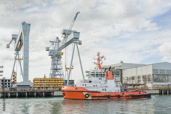 Obraz Tugboat at work at a shipyard with cranes in the background
