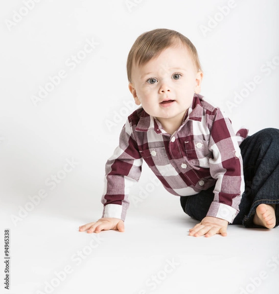 Fototapeta a cute 1 year old baby stands in white studio with jeans and a red white flannel looking camera left in excitement