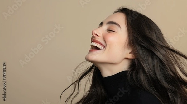 Obraz A young woman with long dark hair, laughing with joy. Her hair flows freely as she smiles, creating a dynamic and happy atmosphere against a neutral background.