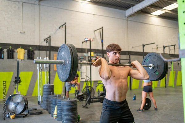 Obraz Young man lifting barbell in gym with focused expression