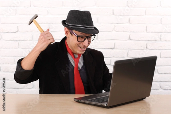 Fototapeta Furious angry man destroying his laptop with a hammer. Bad news computer